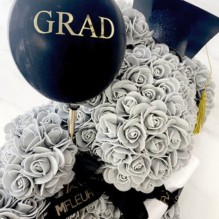 A photo of a gray rose bear with black balloon with GRAD words written.